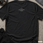 Uncharted Tribe Network — Cyber Tee in Black Heather, back view showing the small Uncharted Tribe Collective logo below the rear neckline on a flat-laid T-shirt.